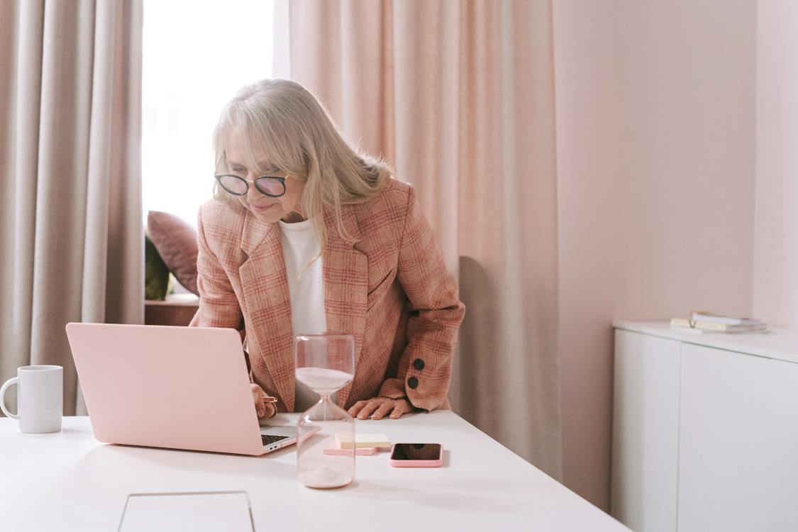 Free An Elderly Woman in Pink Blazer Wearing Eyeglasses while Looking at the Laptop Stock Photo
